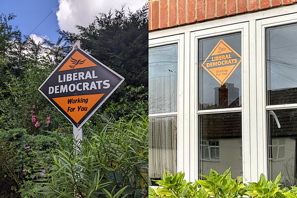 Two Lib Dem diamond posters, one in a garden and one in a window